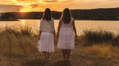 İki kadın beyaz elbise ve fener sırtlarında gün batımını izlemek