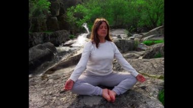 Kadının arkasında bir nehirde bir şelale ile yoga yapıyor