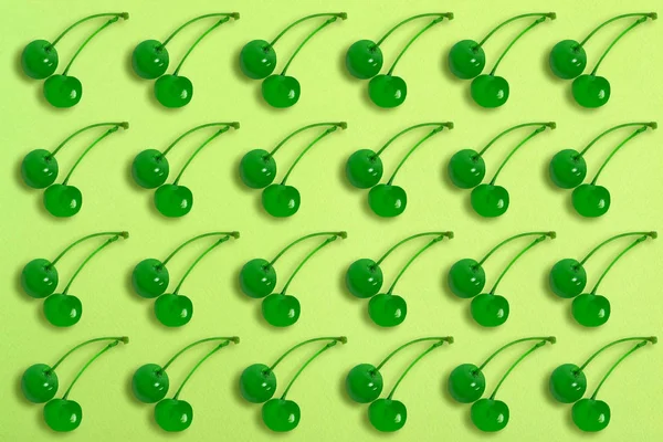 Green maraschino cherries on lime paper background. Cherry pattern. Trendy flat lay, minimal style. Bright summer food background