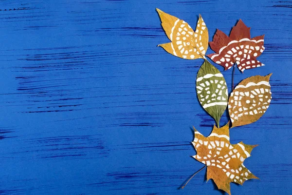 Hand-painted on dry autumn leaves by dint of paper lace napkin. Children's art project. DIY concept. Step by step photo instructions. Step 4. Finished painted leaves on blue background with copy space