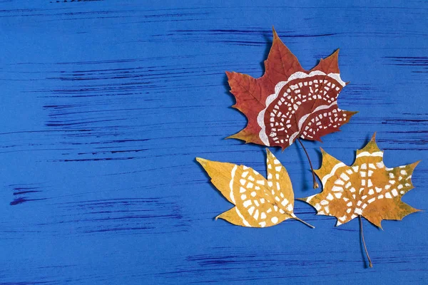Hand-painted on dry autumn leaves by dint of paper lace napkin. Children's art project. DIY concept. Step by step photo instructions. Step 4. Finished painted leaves on blue background with copy space