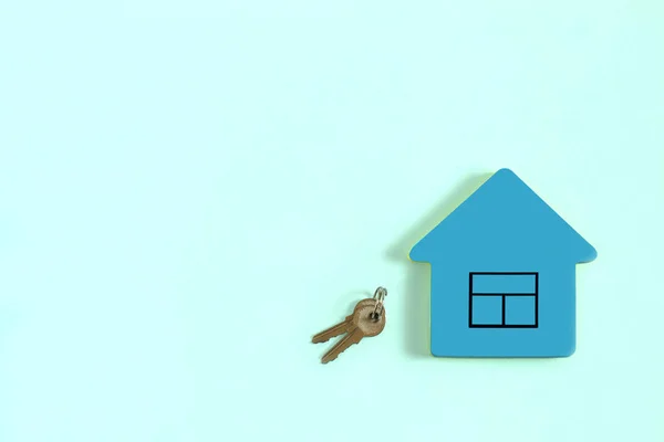 Blue block of paper for notes in shape of house with picture window and keys on pastel blue background. Minimal style. Concept of sale or purchase of real estate. Copy space