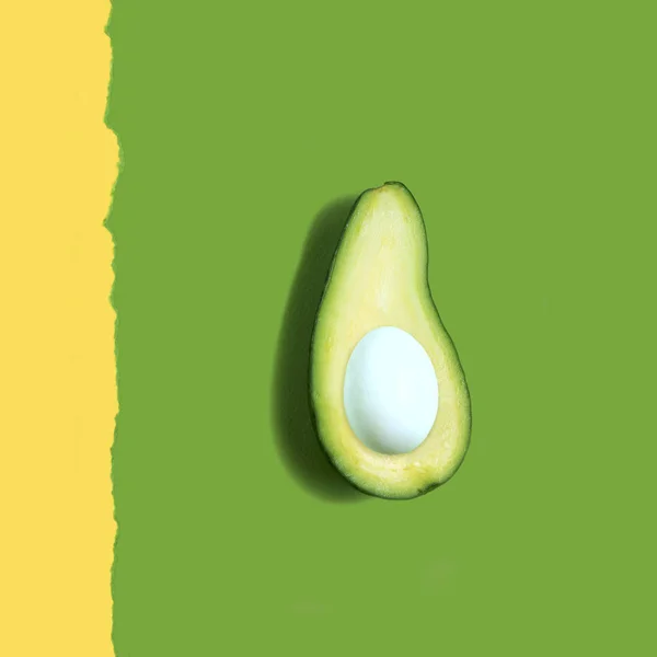 Avocado with egg instead of seed on a two-color paper background. Photo manipulation with similar forms. Creative idea, imagination and fantasy. Minimal style