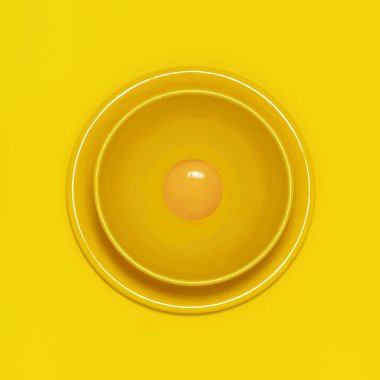 Çiğ tavuk yumurta sarısı sarı plaka ve sarı zemin üzerine sarı kase. Kare tek renkli görüntü
