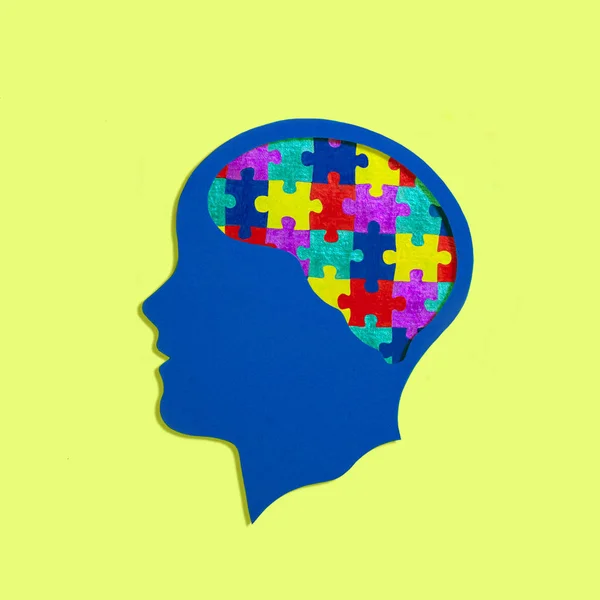 Stylized head silhouette. Multi-colored puzzles instead of brain. Symbol of autism, problems with social interaction and communication. Concept of mental health and disease