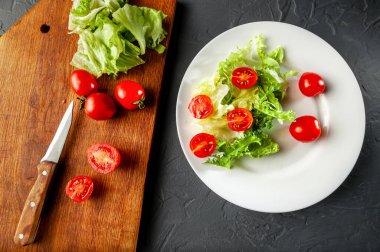 Diyet ve bıçak sürecinde salata yapma süreci kiraz domatesli, salatalı, düz ve üst manzaralı ahşap bir tahtanın üzerinde yatar. Gri ve koyu arkaplan