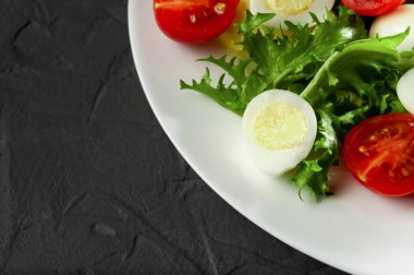 Taze sebzeli salata ve gri arka planda beyaz bir tabakta bıldırcın yumurtası, makro çekim, üst manzara.