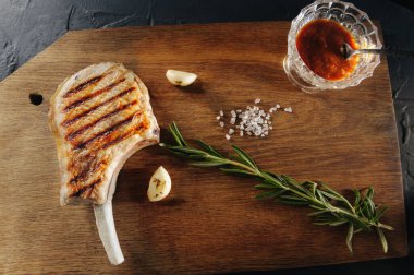 Kemiğin üstünde ızgara biftek, sarımsak ve ahşap bir tahtanın üstünde kaba tuz.