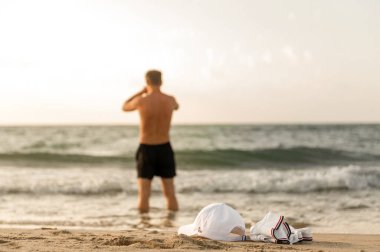 Bir adam, beyaz tişörtü ve şapkasıyla denizde yüzmeye gider.