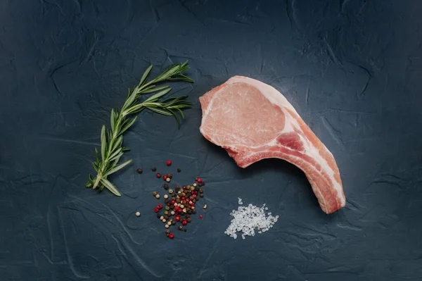 Trozo de carne cruda para filetes, costilla de hueso con sal marina y especias sobre un fondo azul oscuro, vista superior y puesta plana — Foto de Stock