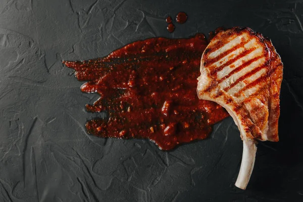 Foto conceptual de matar a un animal. Filete asado en el hueso con el efecto de la sangre sobre un fondo gris. Vista superior y plano laico — Foto de Stock