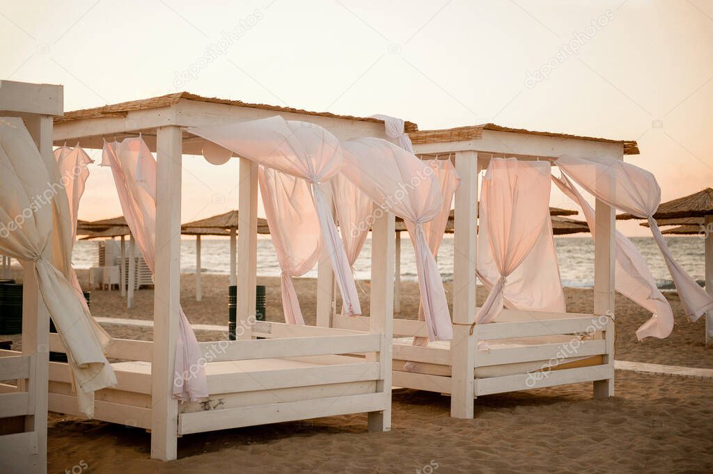 a few gazebos on the beach at sunset with evolving curtains, without people