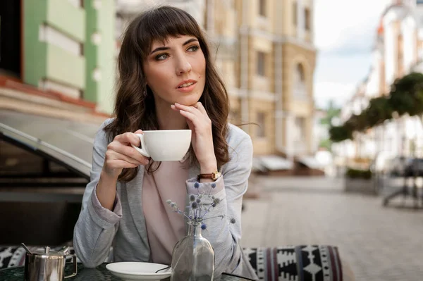 Kahve fincanı taşıyan güzel genç bir kadın kahve dükkanına bakıyor.
