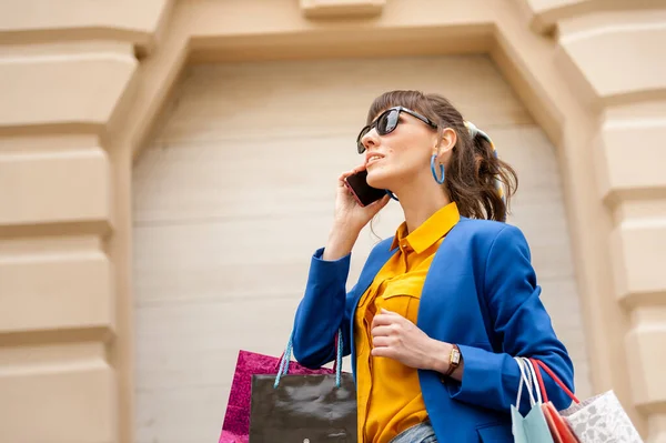 Busy girl holds a lot of packages and a mobile phone on a bright background