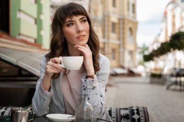 Kahve fincanı taşıyan güzel genç bir kadın kahve dükkanına bakıyor.