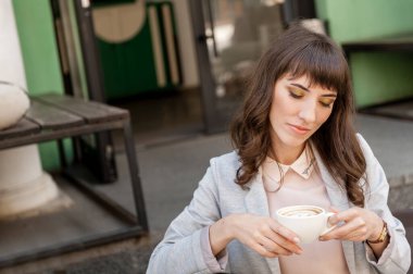 Genç bir kız bir fincan kahveyle düşünceli bir şekilde bir kafede oturuyor.