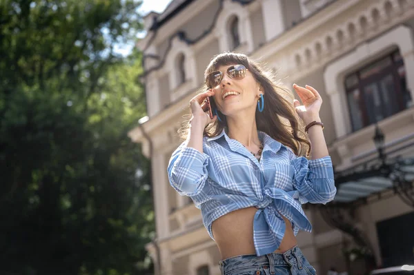 Портрет жінки в сонцезахисних окулярах. Молода дівчина в блакитній сорочці в окулярах говорить по телефону в центрі міста — стокове фото