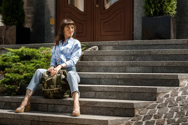 A tourist girl sits on the steps in the city center with a backpack — Stock Photo, Image