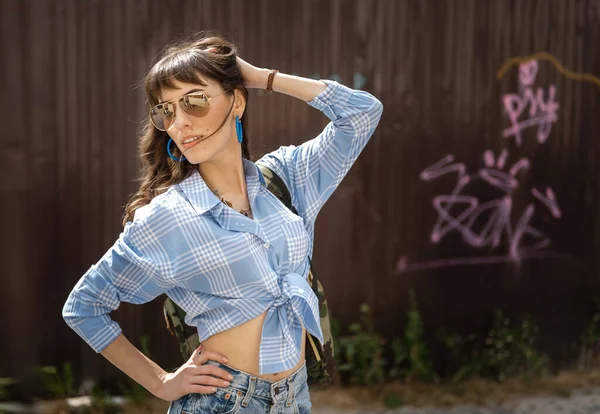 Girl in glasses and blue shirt poses against the background of a brown wall — Stock Photo, Image