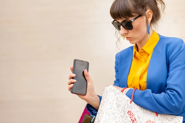 Busy girl holds a lot of packages and a mobile phone on a bright background