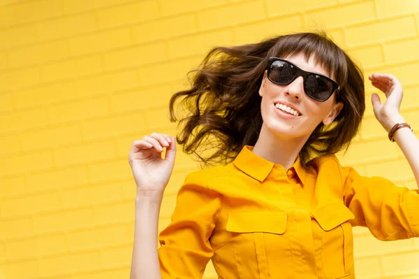 Happy girl in bright clothes on a yellow background enjoys life. Girls hair develops in the wind — Stock Photo, Image