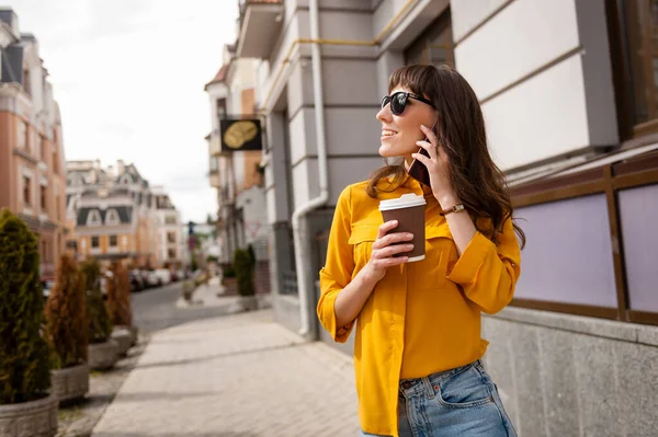 Молода дівчина розмовляє по телефону з чашкою кави в руці — стокове фото