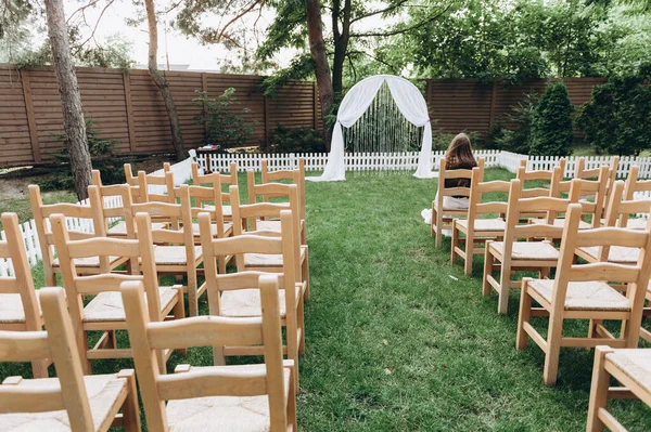 Wedding ceremony in the style of Rustic. Wooden chairs and a white arch. On the chair sits the first guest and waits for the beginning — Stock Photo, Image