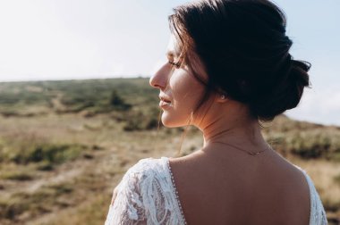 Şık gelin, gün batımında dağların güzel manzarasında ayakta duruyor.