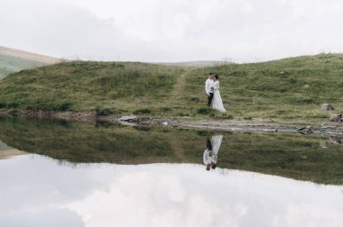 Yeni evliler göl kenarındaki dağlarda yürür.