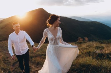 Gelin ve damat gün batımında dağlarda bir düğün yürüyüşünde.