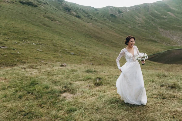 Gelin gölün yanındaki dağlarda. Gelin uzun bir gelinlik giyiyor, dantelli ve arkası açık.