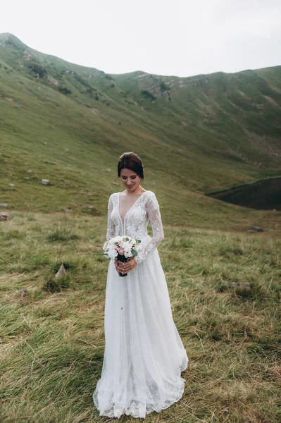Невеста в горах возле озера. На невесте длинное свадебное платье с кружевом и открытой спиной — стоковое фото
