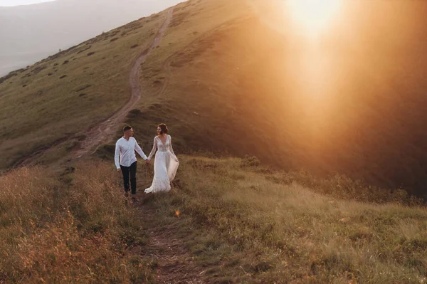 Жених и невеста ходят руками по горной дороге на закате — стоковое фото