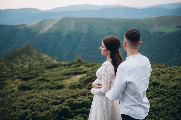 Genç gelin şık bir damada yaslanıyor ve ayakta duruyor. Doğada sarılan yeni evli bir çift.