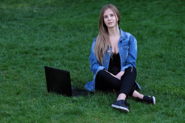 çimenlerin üzerine oturmuş bir dizüstü bilgisayar ile kız