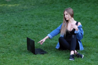 çimenlerin üzerine oturmuş bir dizüstü bilgisayar ile kız