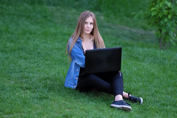 çimenlerin üzerine oturmuş bir dizüstü bilgisayar ile kız