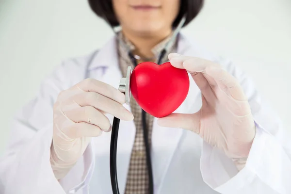 Female doctor holding a stethoscope check up on a red heart ball
