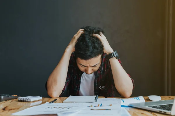 Homme stressé.Un jeune homme assis à son bureau et tient la main sur — Photo