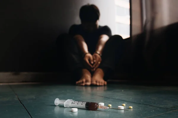 注射器和药物与焦点外的人坐在地板上和汉 — 图库照片