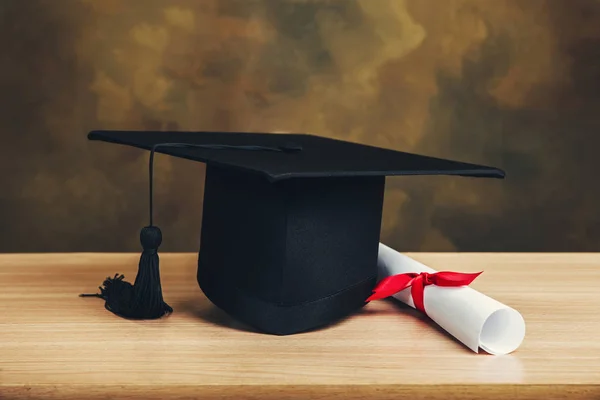 Graduation concept.graduation cap, hat with degree paper on wood