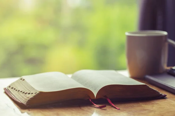 Open bible with a cup of coffee for morning devotion on wooden