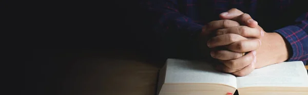 Les mains du jeune homme en prière et la Bible sur une table en bois . — Photo