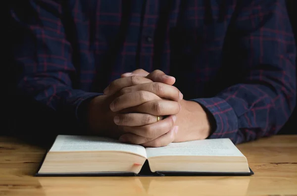 Mains d'un jeune homme pliées priant pour une Bible sur une table en bois — Photo
