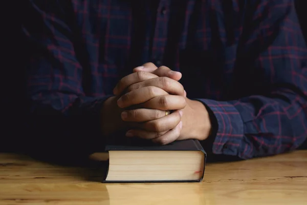 Kezében imádkozó fiatalember és a Biblia egy fából készült asztal. — Stock Fotó