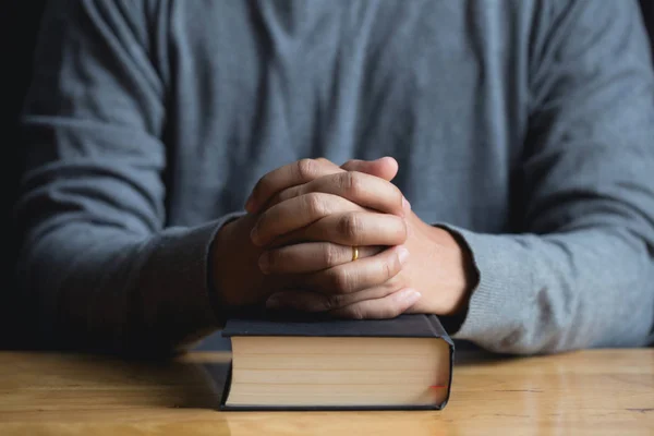 Gebetshände eines jungen Mannes legen auf eine Bibel, die auf einer Holzlasche liegt — Stockfoto