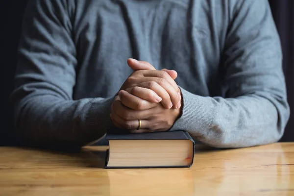 Hands of praying young man and Bible on a wooden table.