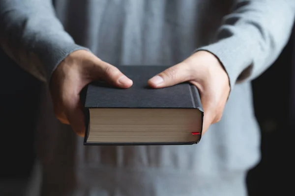 Ręce mężczyzna trzyma czarną książkę. Biblii — Zdjęcie stockowe