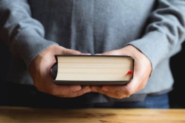 Ahşap masa üzerinde kitap tutan el ele yakın.İncil