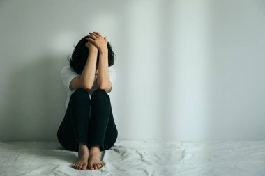 Depresyondaki kadın dizine sarılıp ağlar. Üzgün kadın boş bir odada tek başına oturuyor.. 